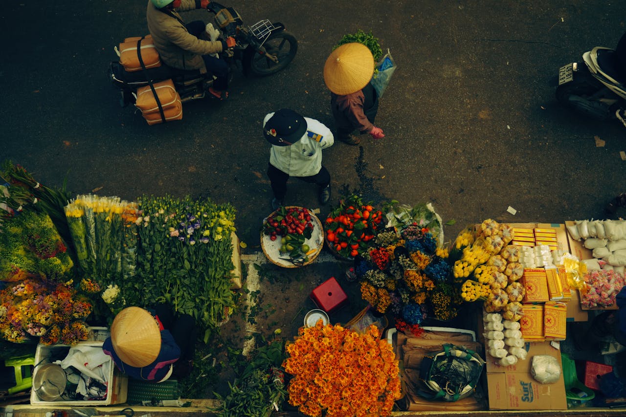 about-me-02 A bustling street market scene with people and colorful flowers viewed from above.